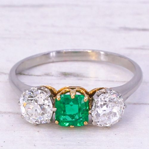 fig 2. An Art Deco three-stone ring featuring a central square-cut green emerald flanked by two round diamonds on a platinum band.