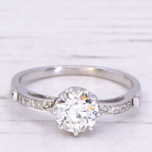 fig 2. An Art Deco diamond engagement ring featuring a central round old cut diamond flanked by diamond-set shoulders on a silver-coloured metal band.