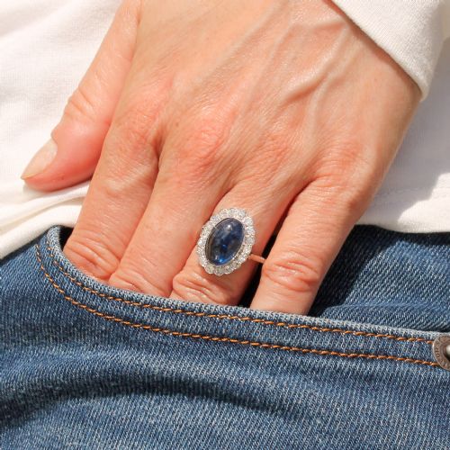 fig 1. An Art Deco ring featuring an oval cabochon blue sapphire surrounded by a halo of diamonds set in a platinum band.