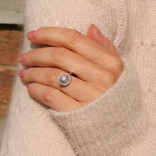 fig 1. An Art Deco diamond cluster ring featuring a central round diamond encircled by a halo of smaller diamonds on a white metal band.