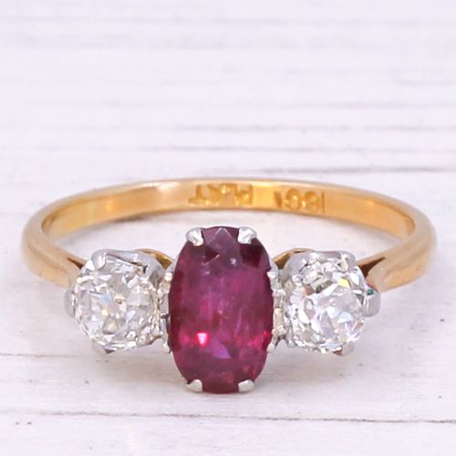 fig 2. An Art Deco three-stone ring featuring a central oval red ruby flanked by two round diamonds on a yellow gold band with platinum claw settings.