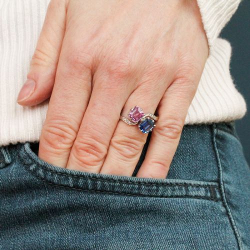 fig 1. An Art Deco platinum crossover ring set with a square-cut blue sapphire and a square-cut pink sapphire flanked by small diamonds on a curved band.