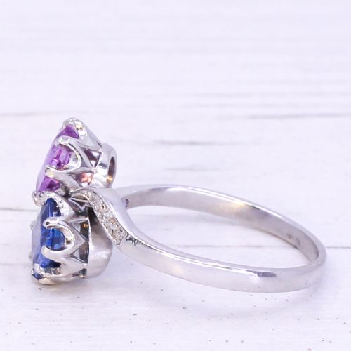 fig 3. An Art Deco platinum crossover ring set with a square-cut blue sapphire and a square-cut pink sapphire flanked by small diamonds on a curved band.