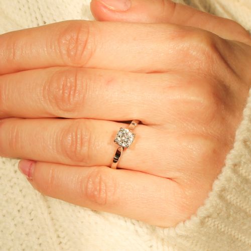 fig 1. An Art Deco diamond solitaire engagement ring featuring a single old-cut diamond set in a four-prong setting with geometric shoulder detail on a silver-tone band.