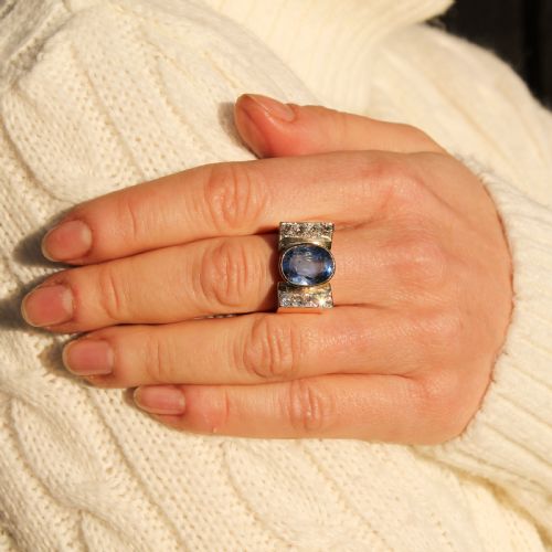 fig 1. A mid-century gold ring featuring a central oval blue sapphire set in a wide band with diamond-set vertical shoulders.