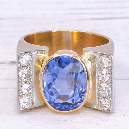 fig 2. A mid-century gold ring featuring a central oval blue sapphire set in a wide band with diamond-set vertical shoulders.