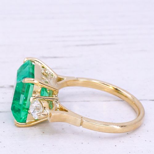 fig 3. An Edwardian yellow gold trilogy ring set with a large square step-cut green emerald flanked by two round diamonds.