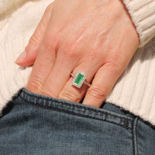 fig 1. A mid-century rectangular emerald cluster ring set in white metal, bordered by small round diamonds with a detailed band.