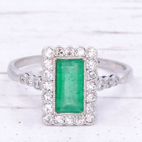 fig 2. A mid-century rectangular emerald cluster ring set in white metal, bordered by small round diamonds with a detailed band.