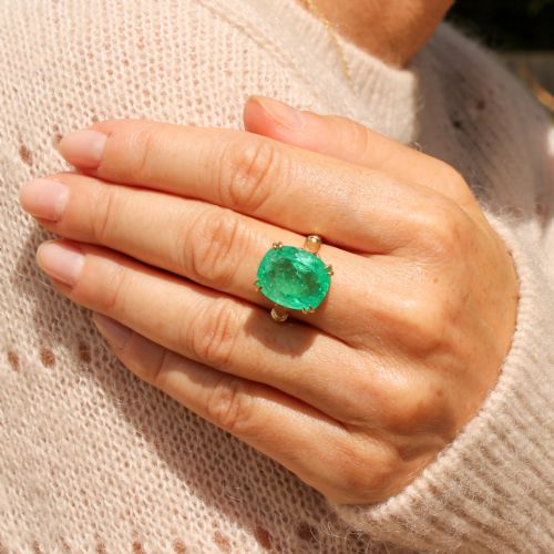 fig 1. A mid-century yellow gold solitaire ring featuring a large cushion-cut green emerald secured with double claw settings.