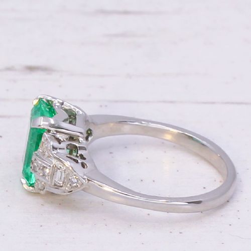 fig 1. An Art Deco platinum ring featuring a central emerald-cut green gemstone flanked by geometric diamond-set shoulders.