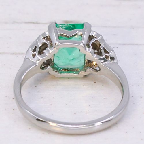fig 3. An Art Deco platinum ring featuring a central emerald-cut green gemstone flanked by geometric diamond-set shoulders.