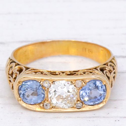 fig 2. An Art Nouveau yellow gold ring set with a central round old cut diamond flanked by two blue sapphires within an openwork scrollwork gallery.