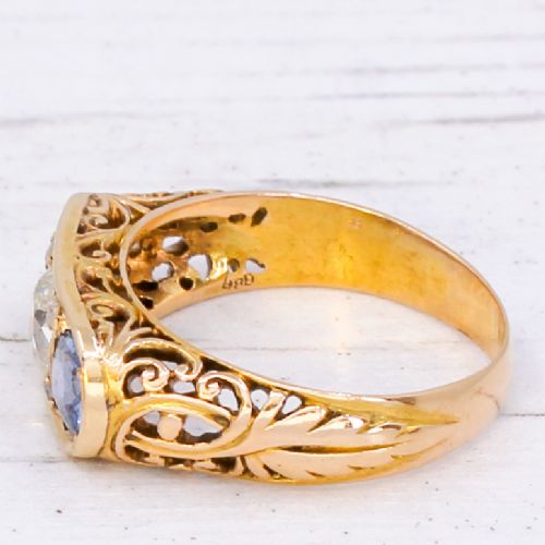 fig 3. An Art Nouveau yellow gold ring set with a central round old cut diamond flanked by two blue sapphires within an openwork scrollwork gallery.