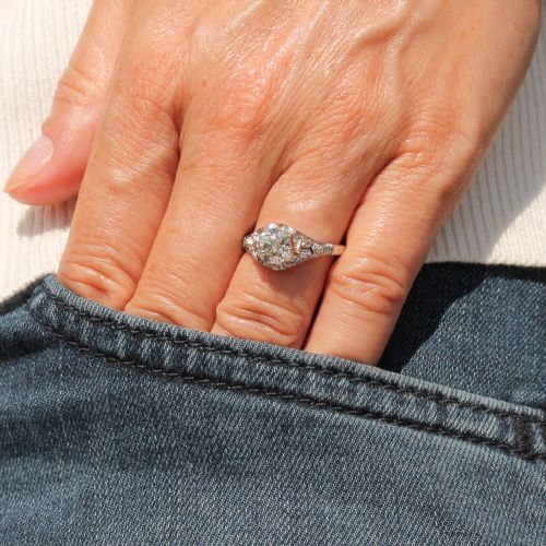 fig 1. An Art Deco style white metal engagement ring featuring a central round old cut diamond flanked by smaller accent diamonds on sculpted shoulders.