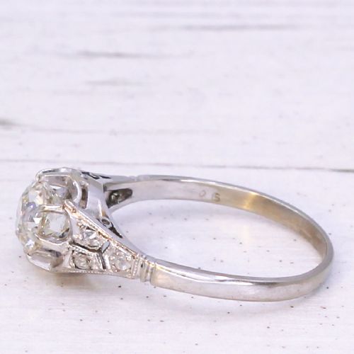 fig 3. An Art Deco style white metal engagement ring featuring a central round old cut diamond flanked by smaller accent diamonds on sculpted shoulders.