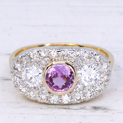 fig 2. A vintage gold ring featuring a central bezel-set pink sapphire flanked by two round diamonds within a pave-set diamond oval plaque.