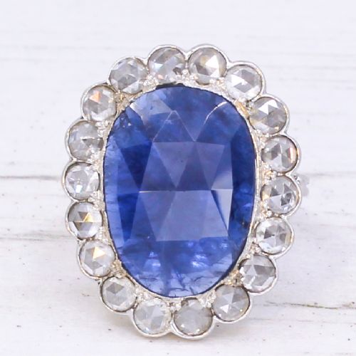 fig 2. An oval blue sapphire gemstone set in a silver-toned metal ring, surrounded by a halo of circular white diamonds.