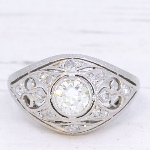 fig 2. An Art Deco platinum ring featuring a central round old cut diamond in a bezel setting surrounded by pierced filigree scrollwork and small accent diamonds.