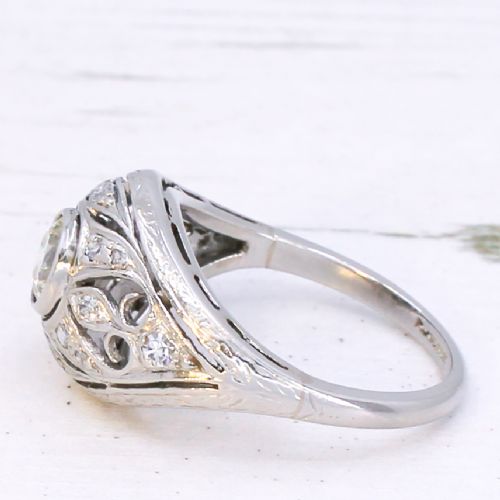 fig 3. An Art Deco platinum ring featuring a central round old cut diamond in a bezel setting surrounded by pierced filigree scrollwork and small accent diamonds.