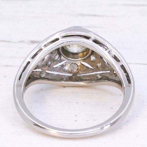 An Art Deco platinum ring featuring a central round old cut diamond in a bezel setting surrounded by pierced filigree scrollwork and small accent diamonds. View V