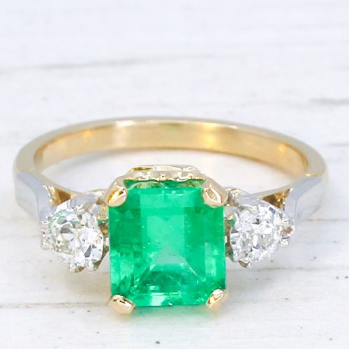 fig 2. A vintage gold ring set with a rectangular central emerald-cut green gemstone and two flanking round brilliant diamonds.