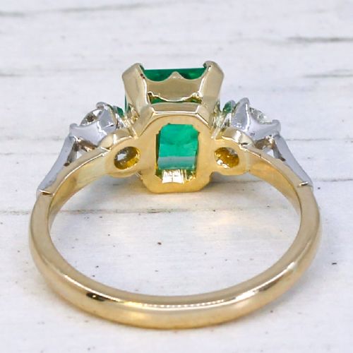 fig 4. A vintage gold ring set with a rectangular central emerald-cut green gemstone and two flanking round brilliant diamonds.