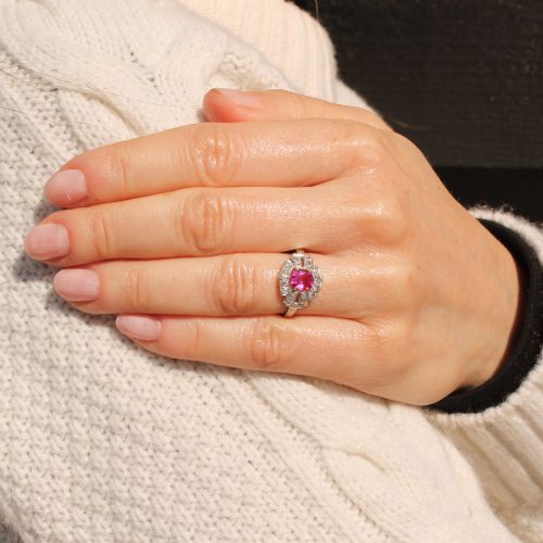 fig 1. An Art Deco platinum ring featuring an oval pink sapphire in a four-claw setting surrounded by a geometric halo of diamonds with milgrain detail.