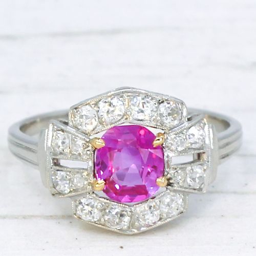 fig 2. An Art Deco platinum ring featuring an oval pink sapphire in a four-claw setting surrounded by a geometric halo of diamonds with milgrain detail.