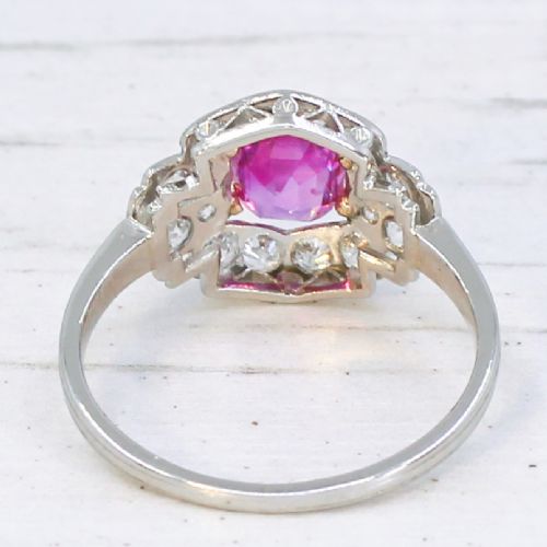 fig 4. An Art Deco platinum ring featuring an oval pink sapphire in a four-claw setting surrounded by a geometric halo of diamonds with milgrain detail.