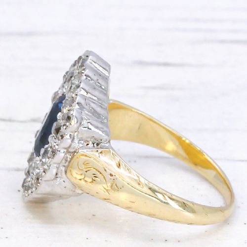 fig 3. An oval blue sapphire surrounded by a double halo of diamonds set in a scalloped white metal mount on an engraved yellow gold band.