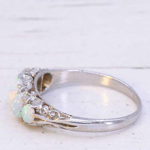fig 3. A white metal ring featuring five graduated oval cabochon opals set in a row across a decorative scrollwork setting.