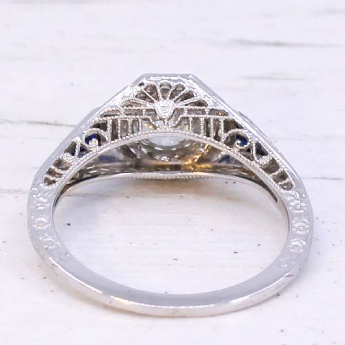 A white metal ring featuring a central old-cut diamond set within an octagonal bezel, flanked by triangular blue sapphires and fine engraved detailing along the band. View V