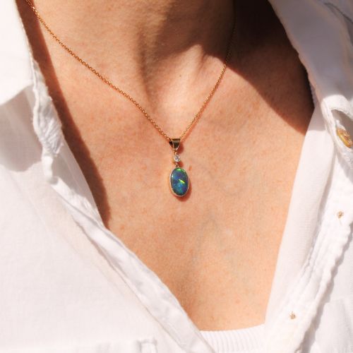 fig 1. An Edwardian black opal and diamond pendant featuring an oval cabochon opal with blue and green play-of-colour mounted in gold below a bezel-set diamond.