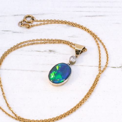 fig 2. An Edwardian black opal and diamond pendant featuring an oval cabochon opal with blue and green play-of-colour mounted in gold below a bezel-set diamond.