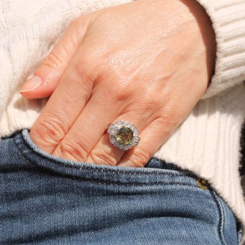 fig 1. A vintage white precious metal ring featuring a central oval green sapphire encircled by a halo of round diamonds and diamond-set shoulders.