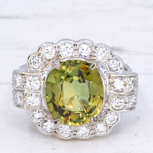 fig 2. A vintage white precious metal ring featuring a central oval green sapphire encircled by a halo of round diamonds and diamond-set shoulders.