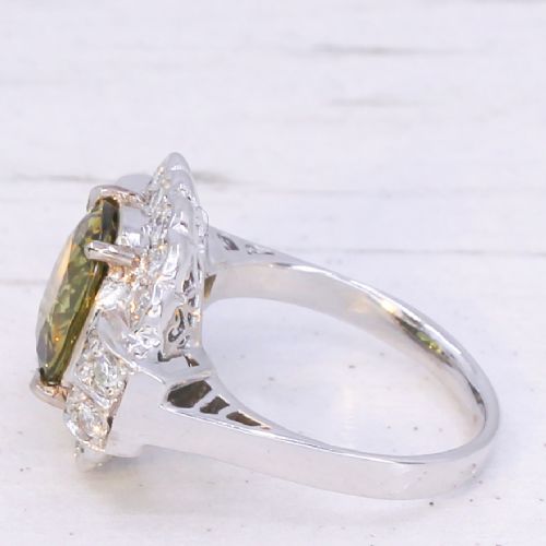 fig 3. A vintage white precious metal ring featuring a central oval green sapphire encircled by a halo of round diamonds and diamond-set shoulders.