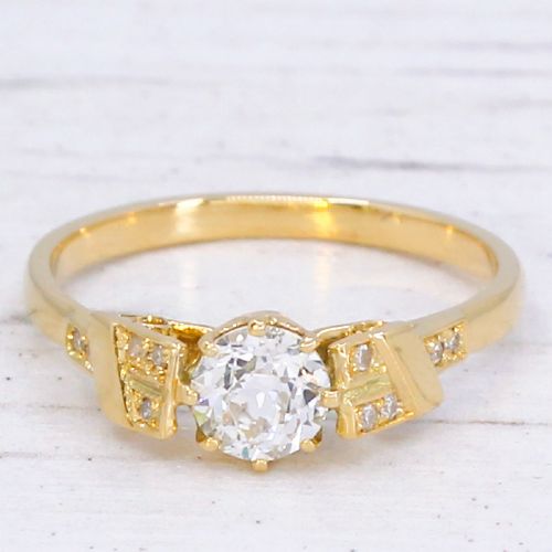fig 2. A yellow gold Art Deco engagement ring featuring a central round old cut diamond flanked by geometric stepped shoulders set with small accent diamonds.