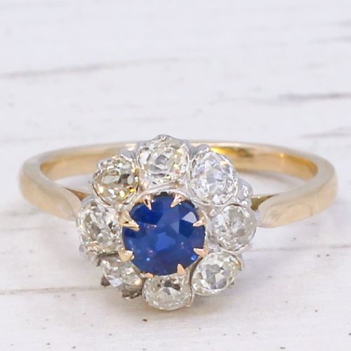 fig 2. A vintage cluster ring featuring a central round blue sapphire encircled by nine brilliant-cut diamonds set on a yellow gold band.