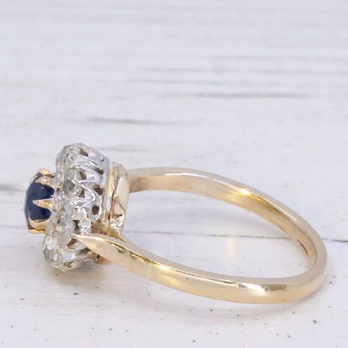 fig 3. A vintage cluster ring featuring a central round blue sapphire encircled by nine brilliant-cut diamonds set on a yellow gold band.
