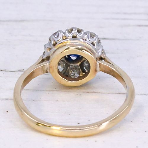 A vintage cluster ring featuring a central round blue sapphire encircled by nine brilliant-cut diamonds set on a yellow gold band. View V