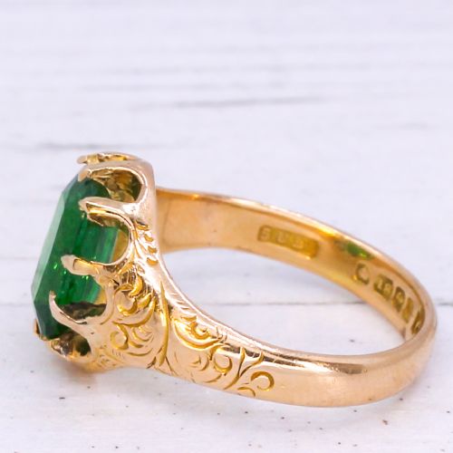 fig 3. An antique gold ring featuring a cushion-cut green tsavorite garnet held in multi-claw settings with scroll-engraved shoulders.