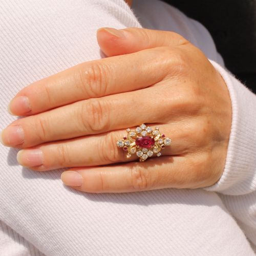 fig 1. A yellow gold vintage ring featuring an oval red ruby surrounded by openwork scroll motifs set with round diamonds and accent rubies.