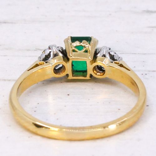A yellow gold band holding a central rectangular green emerald flanked by two round clear diamonds in claw settings. View V