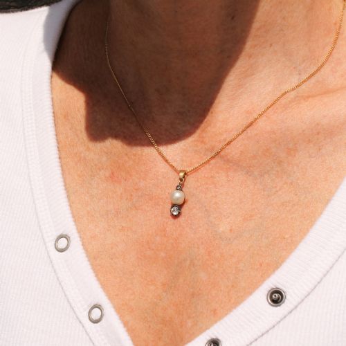 fig 1. An antique gold chain holding a vertical drop pendant featuring a natural pearl suspended between two bezel-set diamonds.