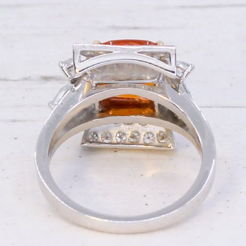 A mid-century vintage cocktail ring featuring a cushion-cut orange garnet central gemstone flanked by pave and marquise diamond accents set in a white gold band. View V