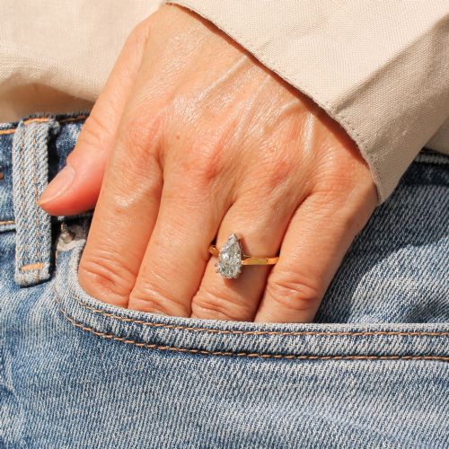 fig 1. A vintage solitaire ring featuring a pear-cut diamond held in white metal claw settings on a smooth yellow gold band.