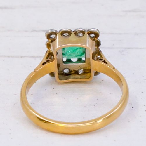 An antique yellow gold ring set with a rectangular central green emerald surrounded by a scalloped halo of small old cut diamonds. View V