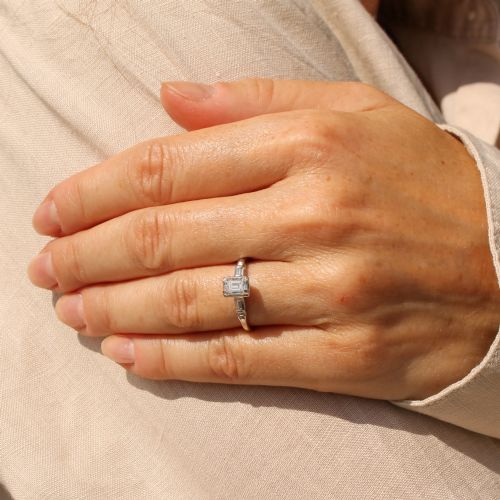 fig 1. A silver-toned metal ring featuring a central rectangular emerald-cut diamond flanked by two baguette-cut diamonds on the shoulders.